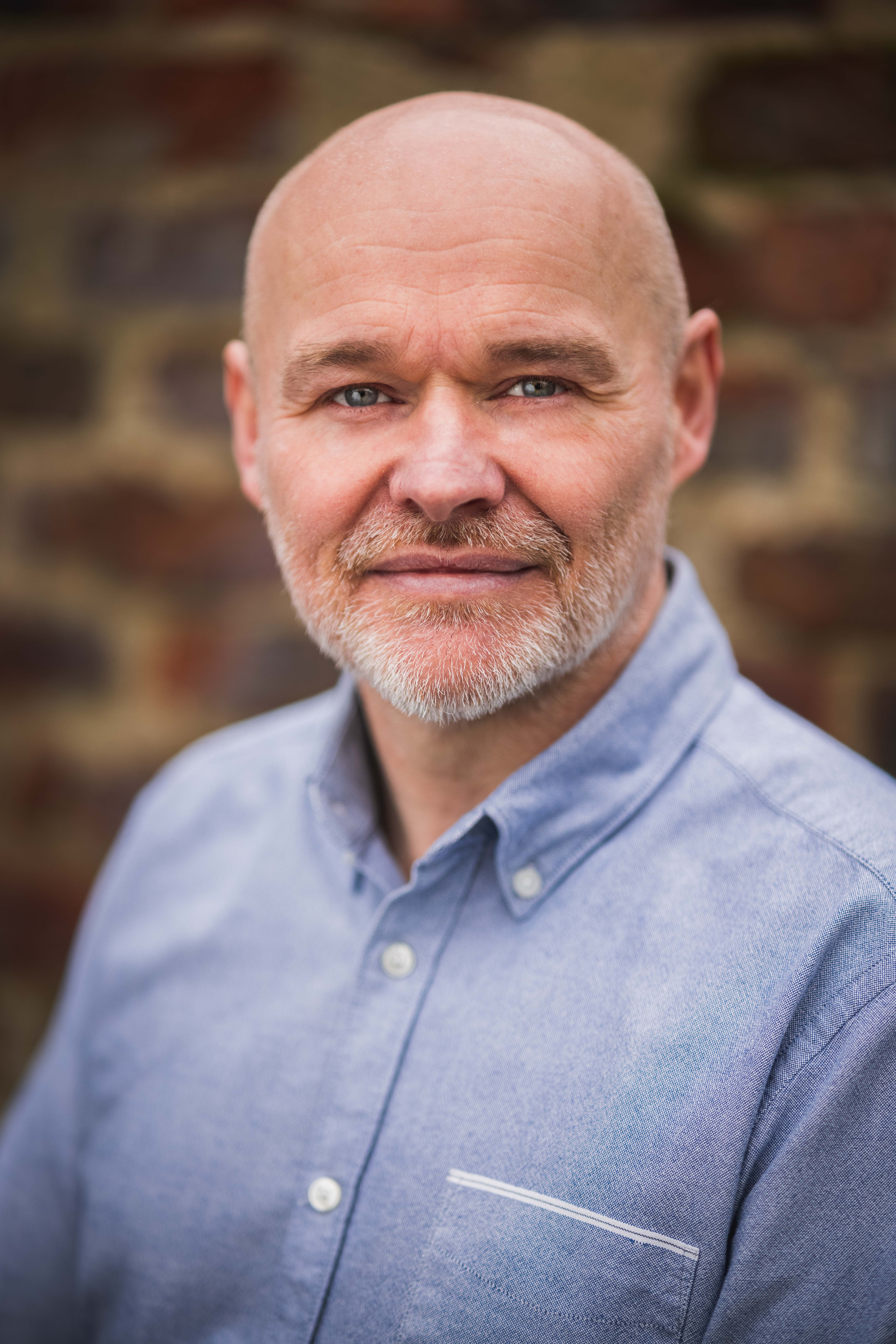 Simon McLaughlin, Founder/Director of Creed Communications. This photograph is a headshot of Simon wearing a blue shirt and a smile