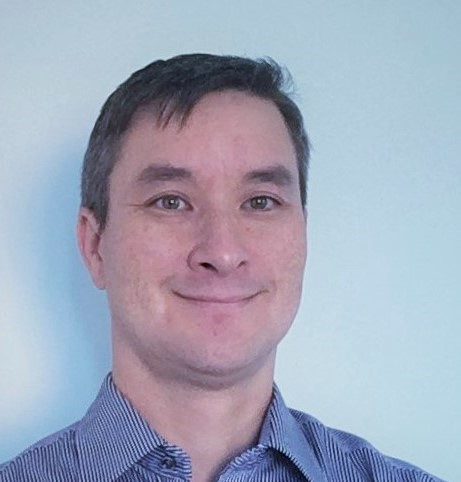 Matthew Brown, CEO and Founder of Adding Value wearing a blue open collared shirt against a pale blue background.