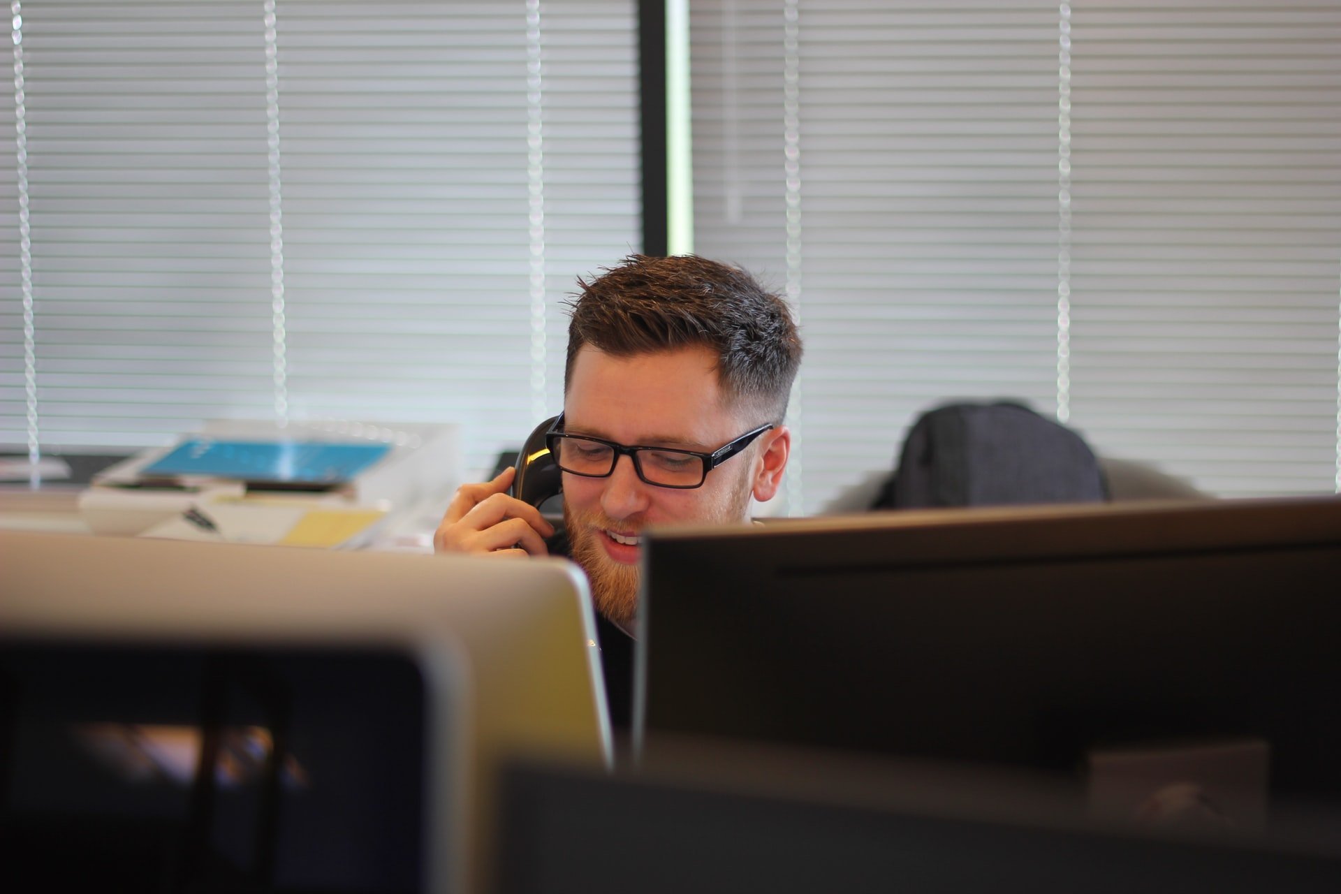 A man behind two computer screens talking on a phone